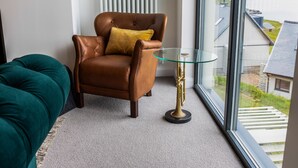 A modern living room with a leather armchair, a glass coffee table, and a teal sofa.