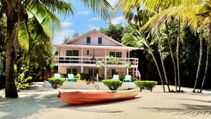 A pink two-story building with a balcony, surrounded by palm trees and a boat in the foreground. - 2BR Beachfront Bungalow-Pool & Oceanfront-Views (Placencia)