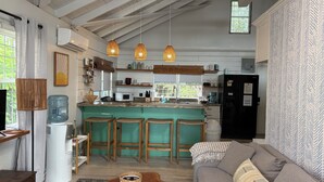 A modern kitchen with a bar area, wooden ceiling beams, and a large water dispenser. - 2BR Beachfront Bungalow-Pool & Oceanfront-Views (Placencia)