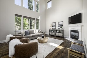 A spacious living room with a high ceiling, large windows, a fireplace, and a flat-screen TV. - Clean, modern, golf course home w/ incredible mtn views, close to hike/golf/ski. (Pleasant Grove)