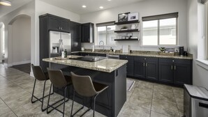 A modern kitchen with dark cabinetry, a stainless steel refrigerator, a granite countertop, and bar stools. - Clean, modern, golf course home w/ incredible mtn views, close to hike/golf/ski. (Pleasant Grove)