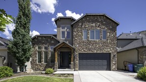 A two-story stone house with a garage, a front porch, and a well-maintained lawn. - Clean, modern, golf course home w/ incredible mtn views, close to hike/golf/ski. (Pleasant Grove)