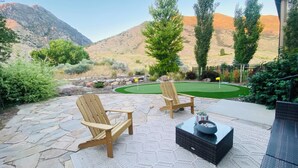 A patio with two wooden Adirondack chairs, a black coffee table, and a putting green. - Clean, modern, golf course home w/ incredible mtn views, close to hike/golf/ski. (Pleasant Grove)