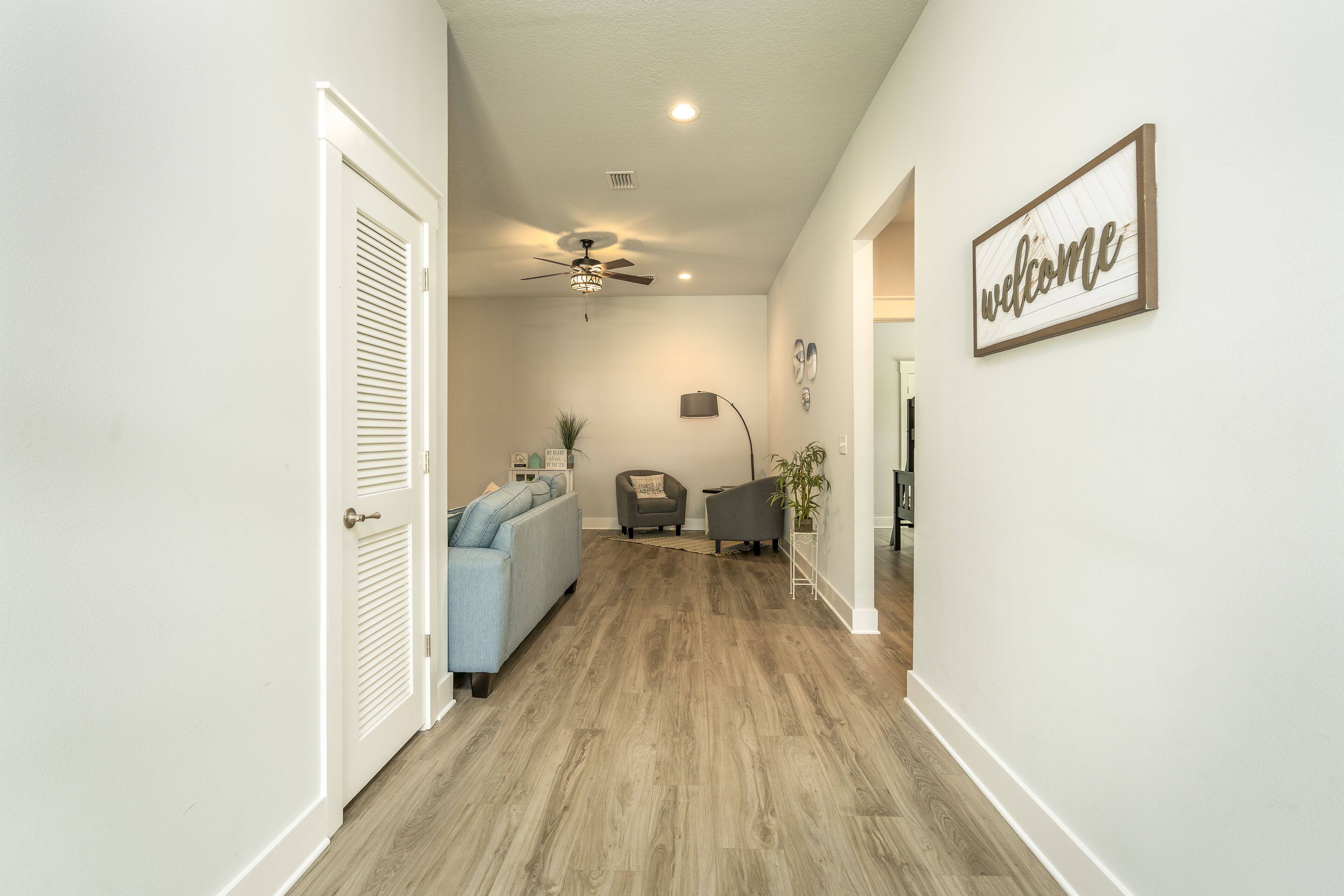 A hallway with a ceiling fan, a 'welcome' sign, a couch, and a chair.