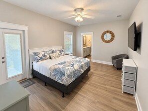 A bedroom with a bed, a desk, a chair, a TV, and a ceiling fan.