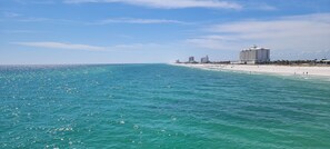Una playa con aguas turquesas cristalinas, una orilla arenosa y un hotel de varios pisos con fachada blanca al fondo.