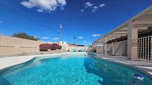 Une piscine d’un bleu éclatant, avec un flotteur à la surface, entourée d’une terrasse en béton et d’une clôture en bois.