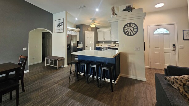 Une cuisine moderne avec un îlot central, des tabourets de bar et une horloge au mur.