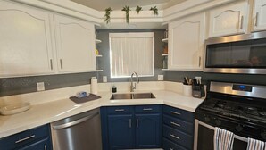 Une cuisine moderne avec des meubles blancs et bleu foncé, des appareils en acier inoxydable et une fenêtre équipée de stores.