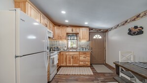 Una cocina con armarios de madera, un refrigerador blanco, una mesa de comedor de madera y una ventana con cortinas.