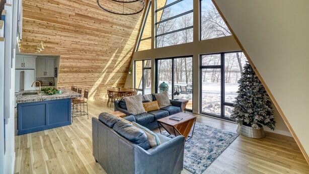 Un loft spacieux avec de hauts plafonds, de grandes fenêtres, un coin salon confortable et une cuisine dotée d’un îlot central bleu.