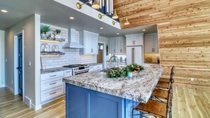 Une cuisine moderne avec des armoires blanches, un îlot en granit et un plafond en bois.