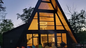 Une maison moderne en bois, de forme triangulaire, dotée de grandes fenêtres et d’un intérieur bien éclairé.