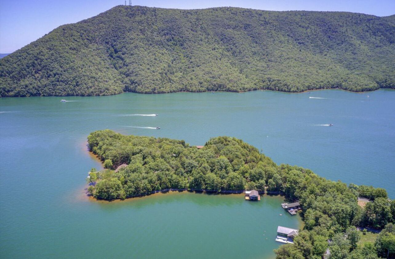 An aerial view of a lake with a small island featuring a dock and a house.