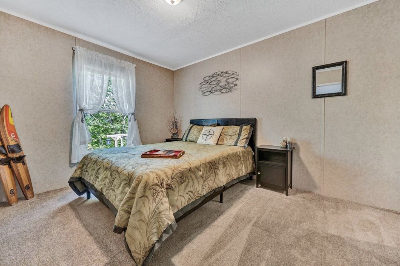 Een slaapkamer met een bed, nachtkastje, raam met gordijnen, wanddecoratie en een spiegel in een lijst.