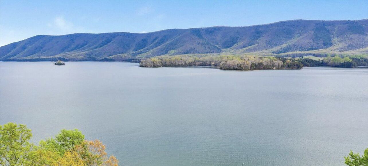 A calm lake with a small island in the center, surrounded by hills and trees.