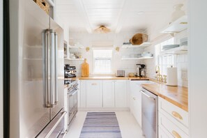A modern kitchen with white cabinetry, stainless steel appliances, and a wooden countertop.