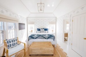 A bedroom with a bed, a chair, a bedside table, a TV, and a door.