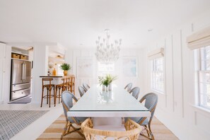 A modern kitchen with white cabinets, a stainless steel refrigerator, and a dining area with a glass table and wicker chairs.