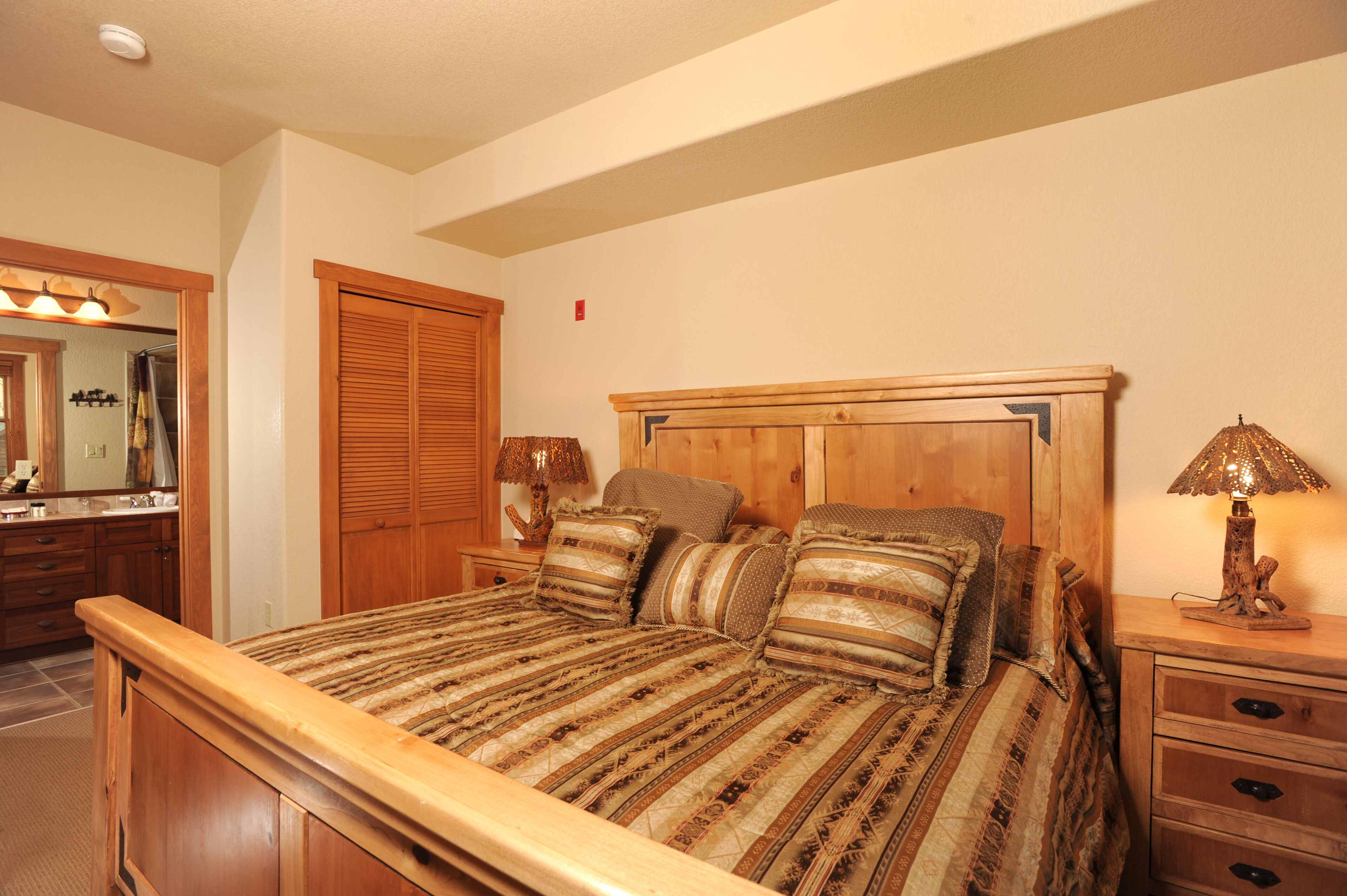 A bedroom with a large bed, wooden headboard, two bedside tables with lamps, a mirror, and a wooden wardrobe.