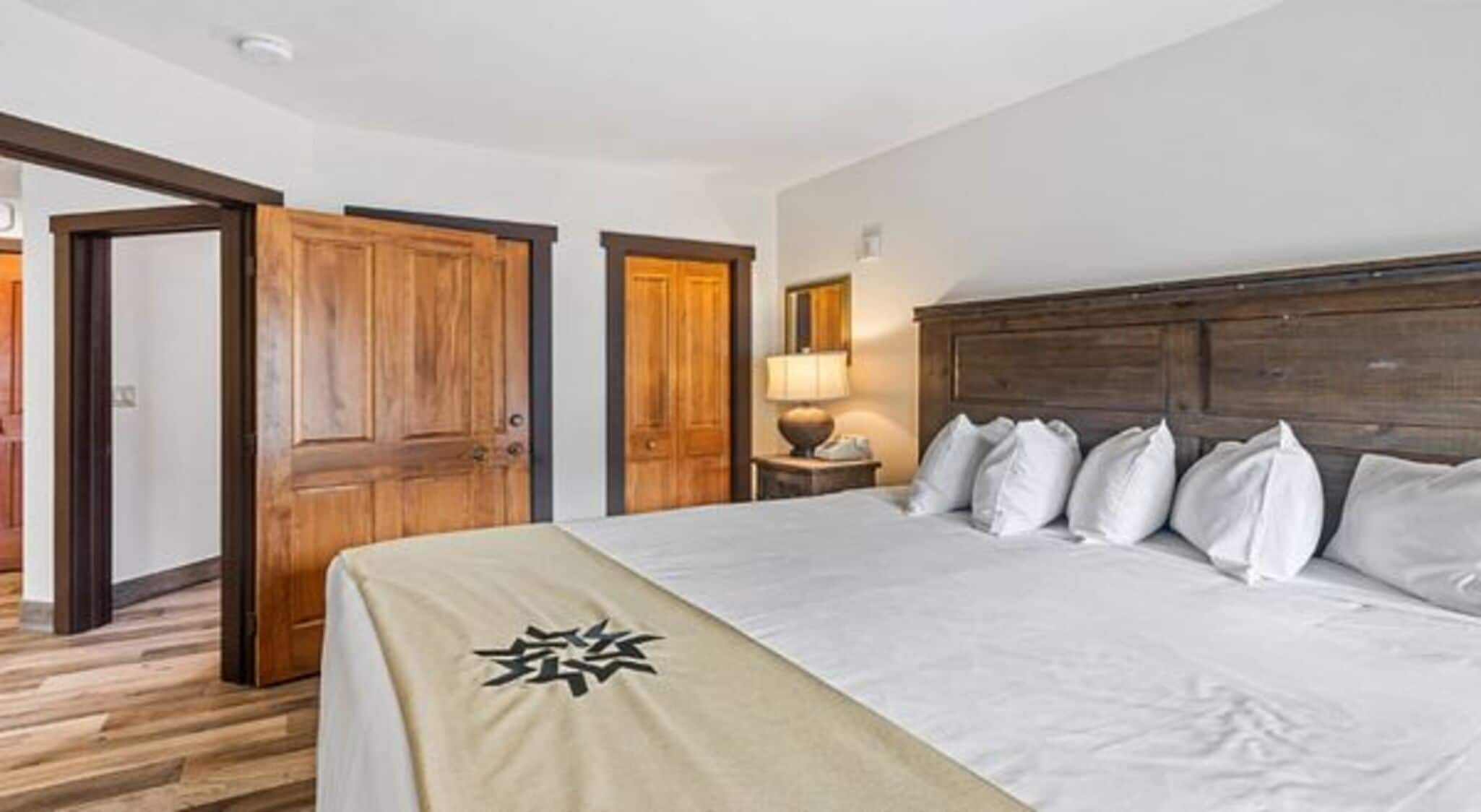 A hotel room with a wooden bed frame, white bedding, and a wooden door.