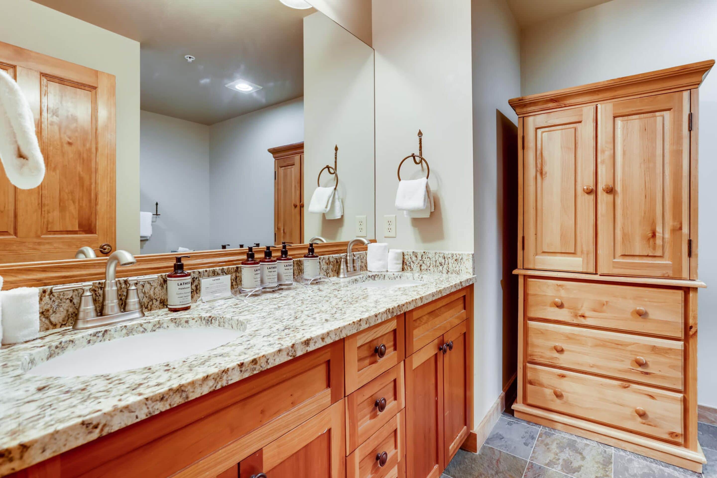 A bathroom with a granite countertop sink, wooden cabinets, a large mirror, and a wooden vanity.