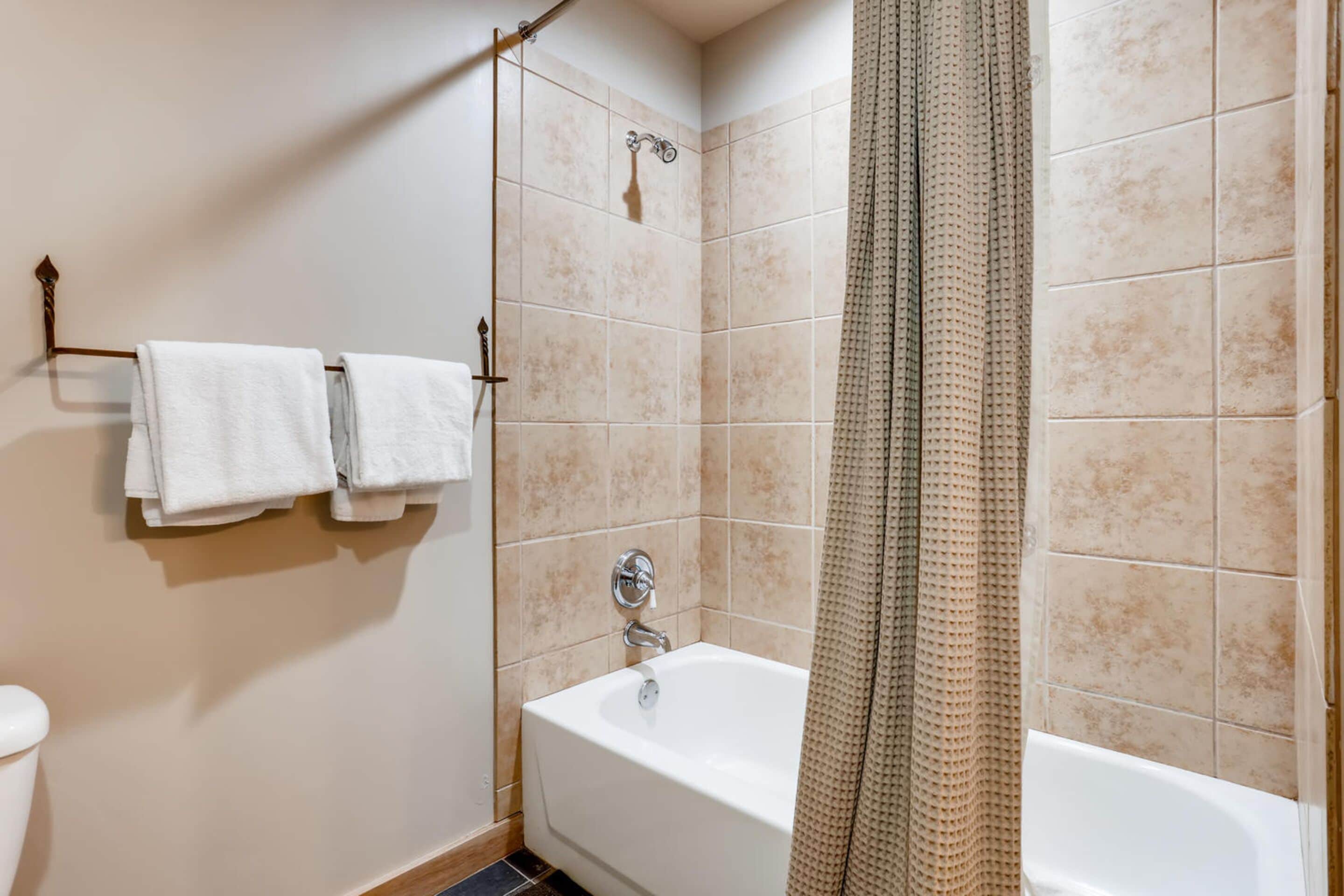 A bathroom with a bathtub, a shower curtain, and two towels hanging on a rack.