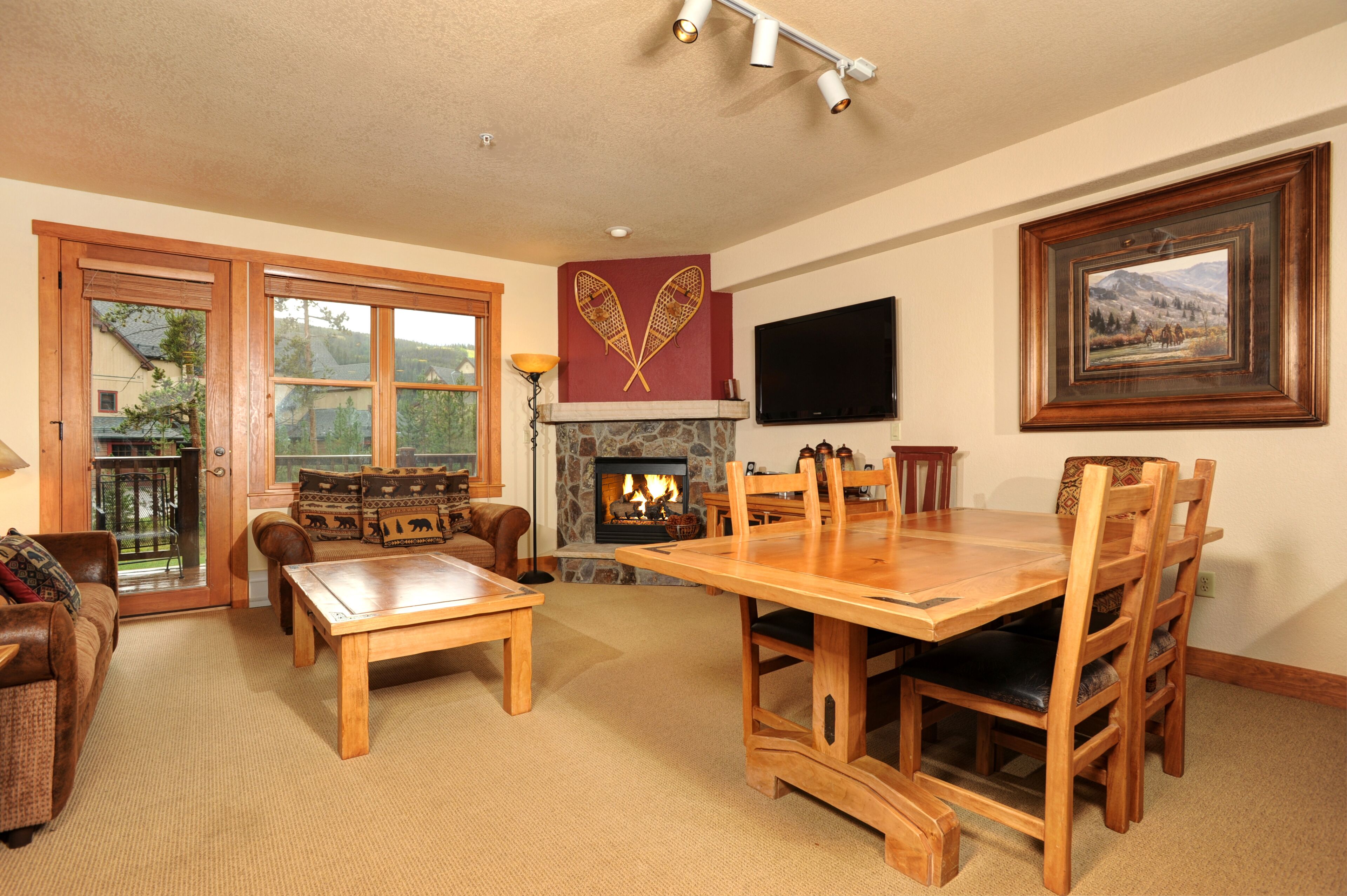 A cozy living room with a fireplace, wooden furniture, and large windows.