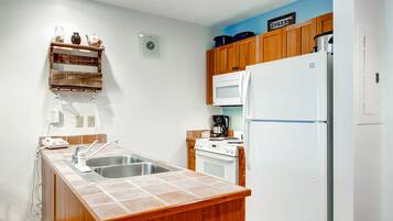 A kitchen with wooden cabinets, a white refrigerator, a microwave, a sink, and a clock on the wall.