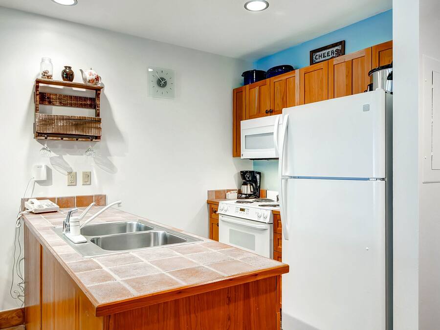 A kitchen with wooden cabinets, a white refrigerator, a microwave, a sink, and a clock on the wall.