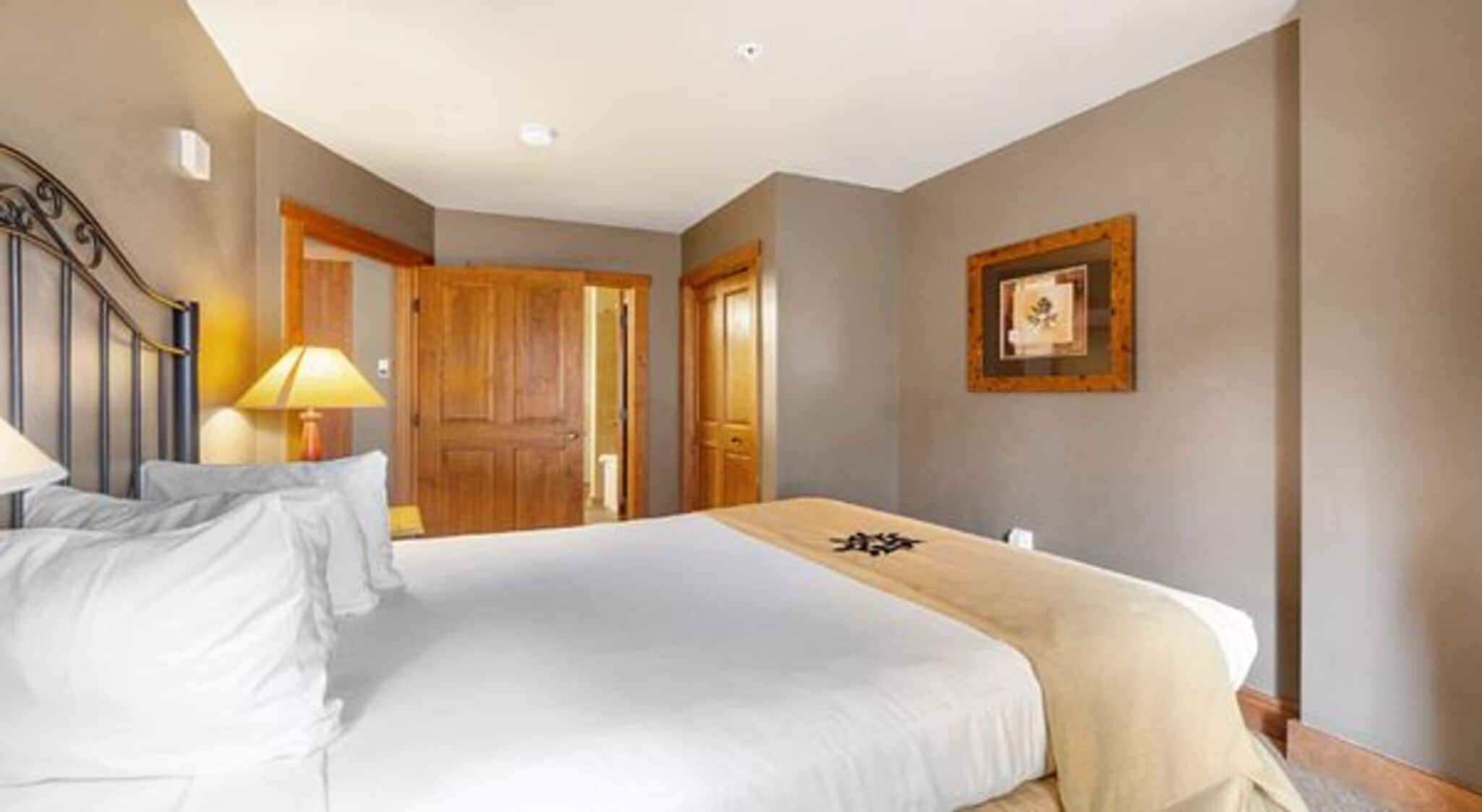 A hotel room with a bed, a desk, a lamp, and a framed picture on the wall.