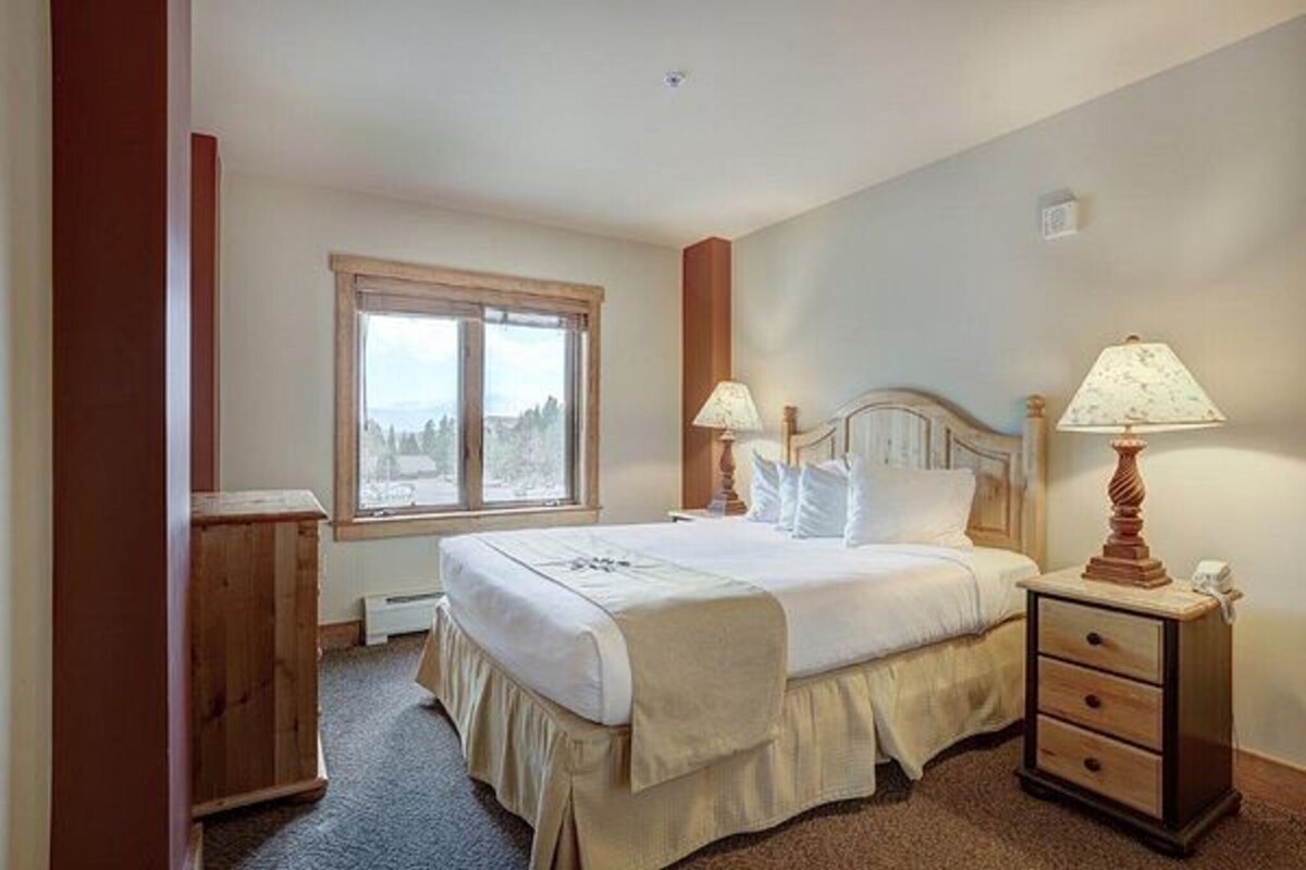 A bedroom with a large bed, two bedside tables, a window, and a view of the outdoors.
