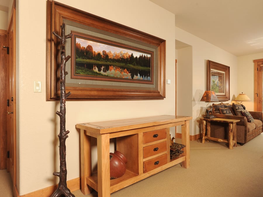 A living room with a wooden console table, a framed landscape painting, a lamp, and a couch with pillows.