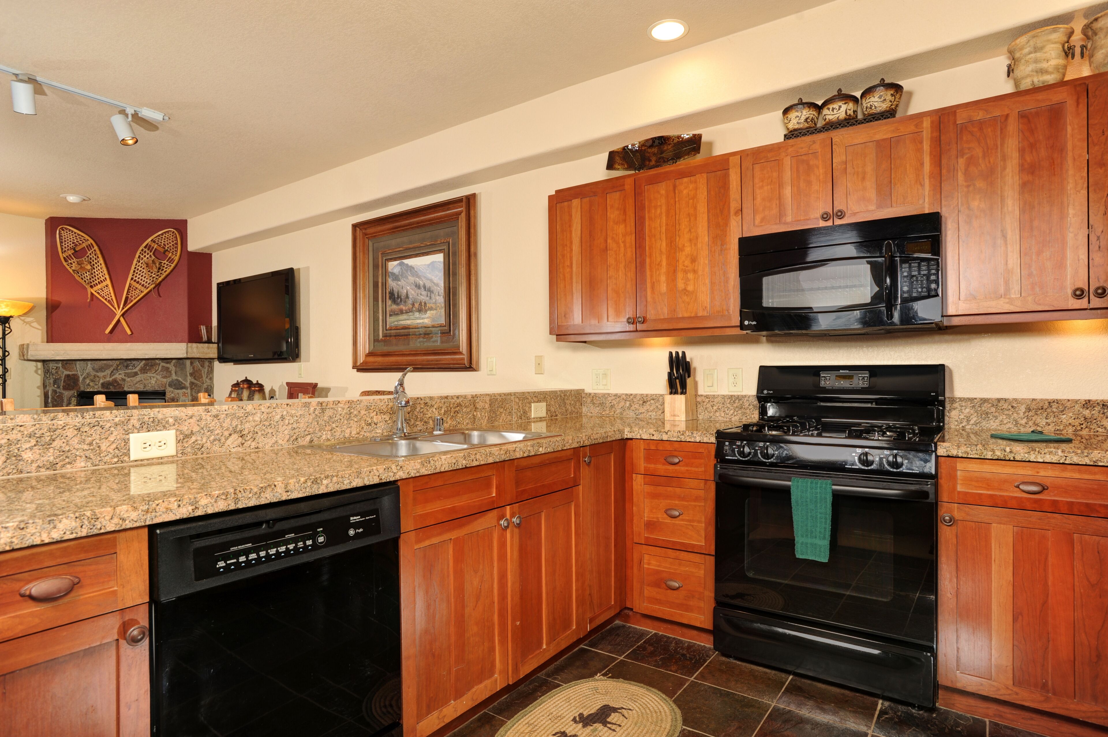 A kitchen with granite countertops, wooden cabinets, a dishwasher, a stove, and a microwave.