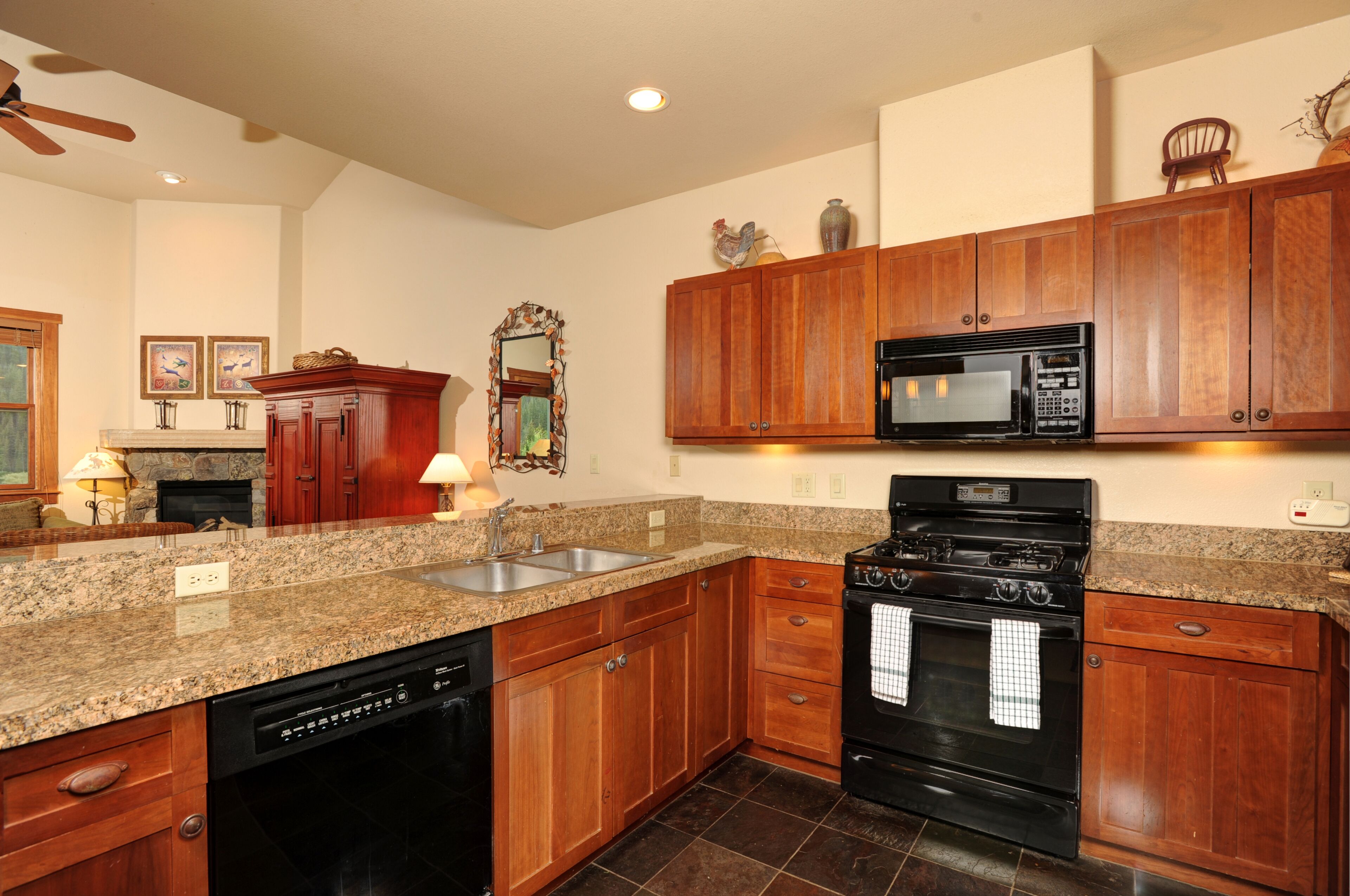 A kitchen with granite countertops, wooden cabinets, a stove, a microwave, and a dishwasher.