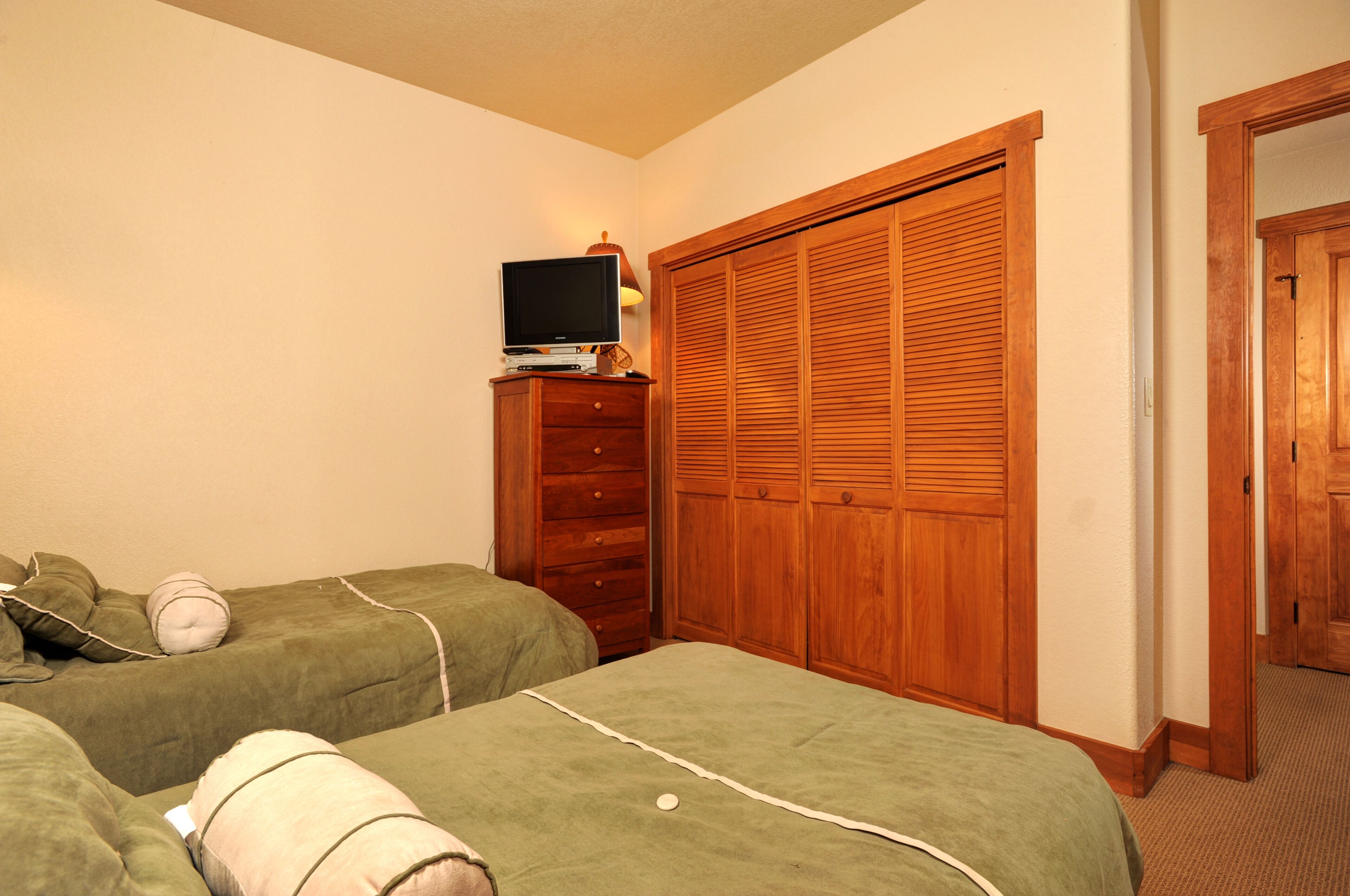 A bedroom with two beds, a TV on a dresser, and a wooden closet.