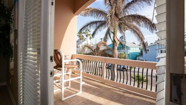 Un balcon avec une chaise blanche, un palmier et une vue sur un quartier résidentiel.