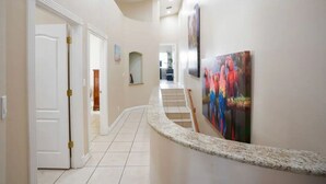 Un couloir doté d’un sol en marbre incurvé, de portes blanches et d’un escalier menant à une autre pièce.