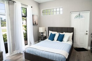 A bedroom with a bed, a nightstand, a window, and a door.