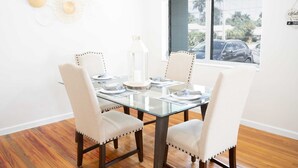 A dining area with a glass table, four upholstered chairs, a white candle, and a decorative wall piece.