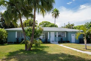 A single-story house with a front porch, surrounded by a well-maintained lawn and palm trees.