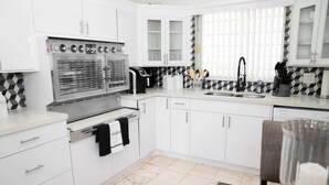 A modern kitchen with white cabinets, a double oven, a sink, and a dining area with a table and chairs.