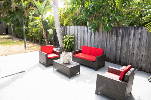 An outdoor patio with wicker furniture and red cushions.