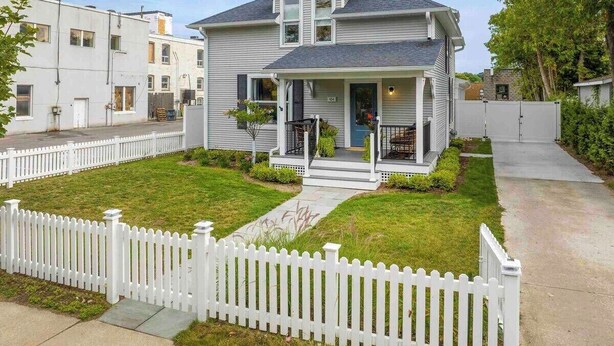 A two-story house with a front porch, a white picket fence, and a well-maintained lawn. - Charlevoix Charm: Boujee Downtown Bungalow (Charlevoix)