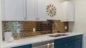 A kitchen with white cabinets, a backsplash with a wood-like pattern, a stainless steel sink, and a dishwasher. - Charlevoix Charm: Boujee Downtown Bungalow (Charlevoix)