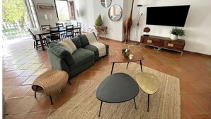 Una sala de estar con sofá, mesa de centro y mueble para televisor. Hay un comedor con mesa y sillas.