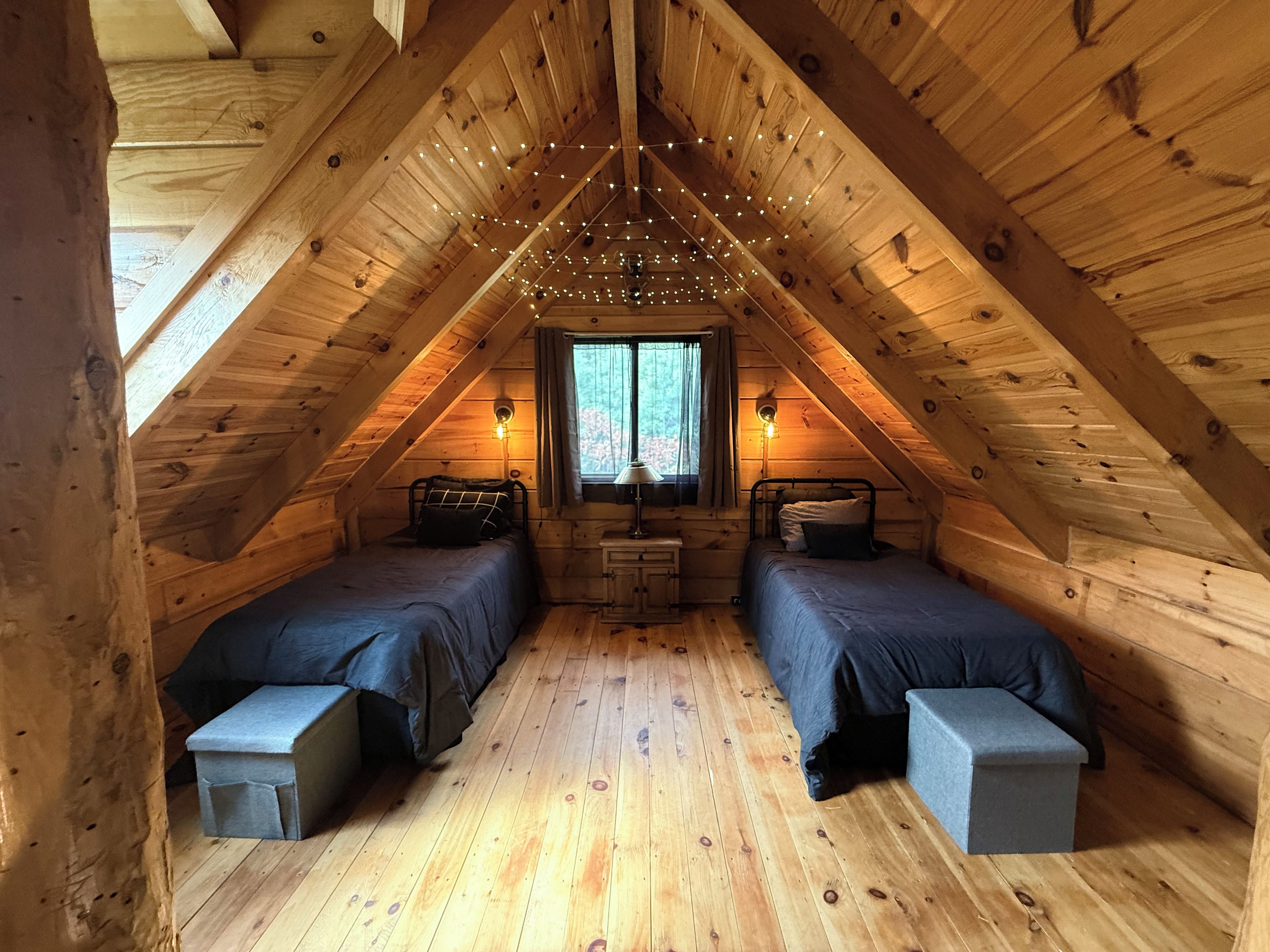 A cozy attic bedroom with two beds, a window, and string lights.