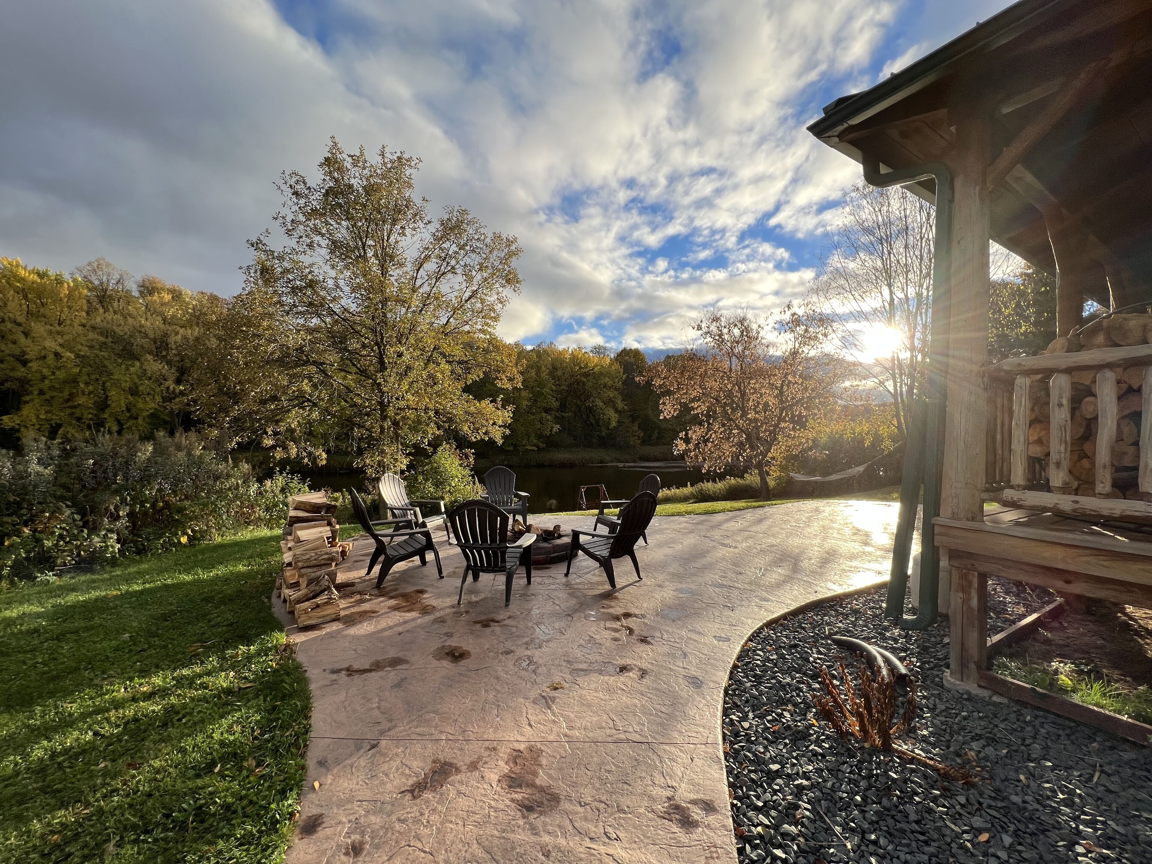 Un patio con sillas Adirondack, un brasero y vistas a un lago y un bosque.