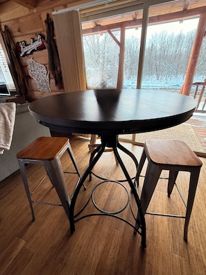 Una mesa redonda con estructura metálica y dos taburetes de madera.