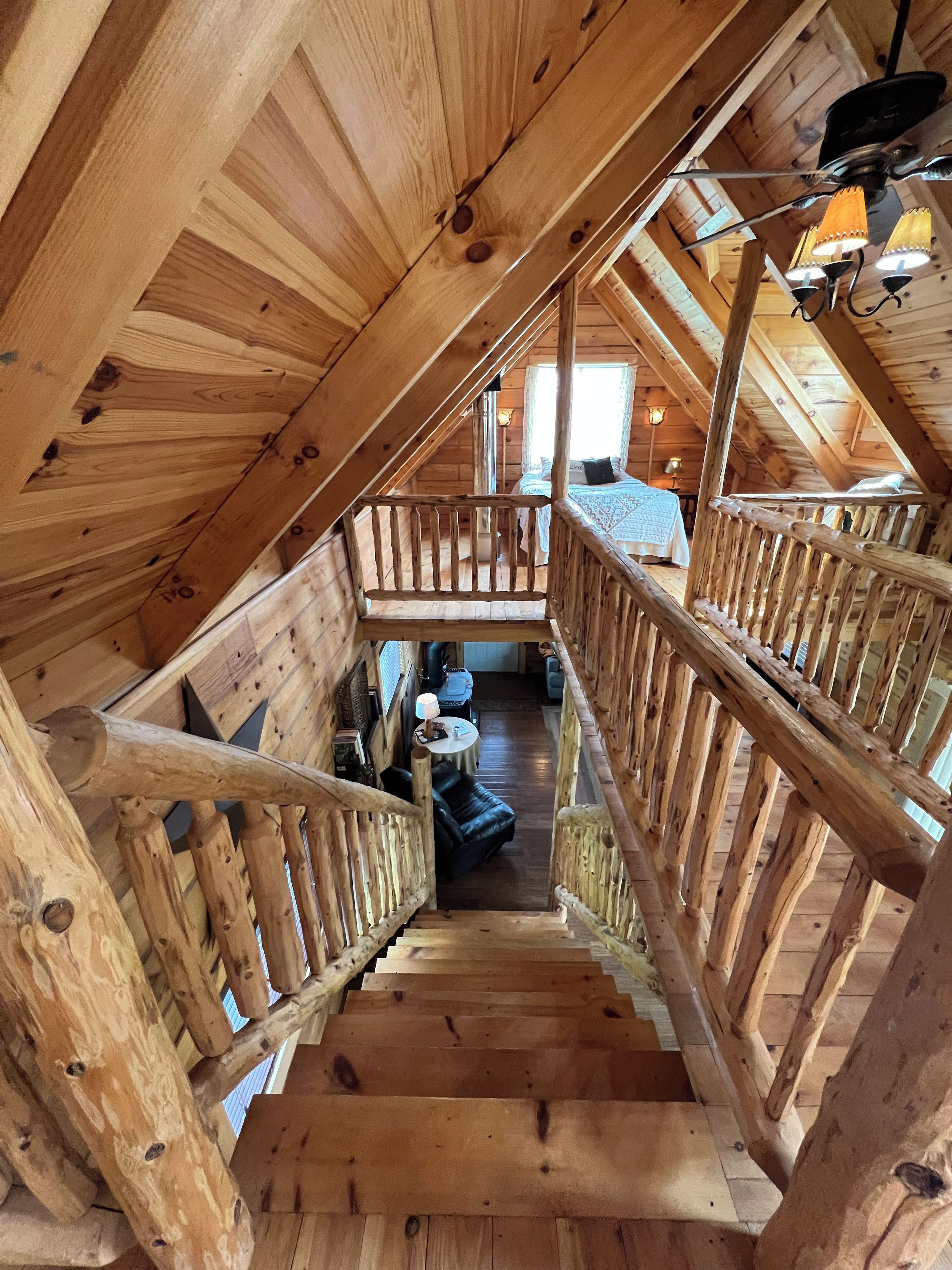 Een houten trap die leidt naar een slaapkamer op een entresol, met een bed, een bureau en een stoel.